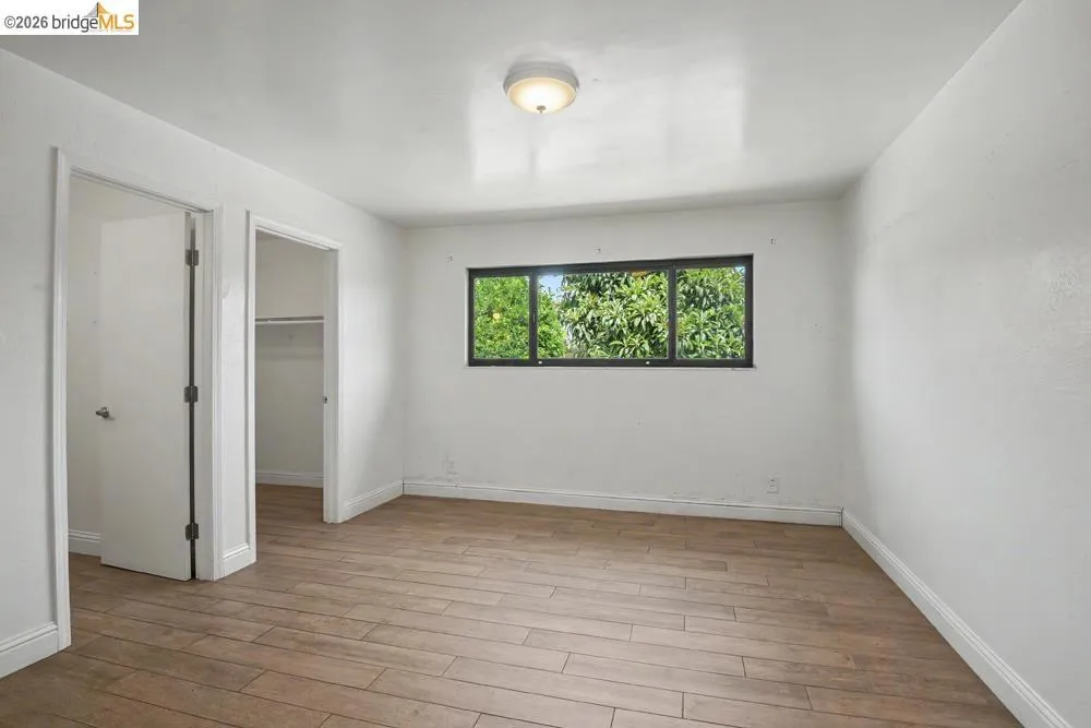 Wood-finish flooring, white walls, and a window with a dark frame