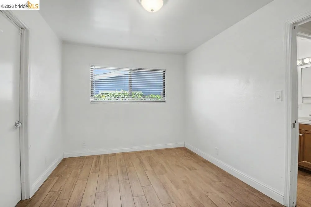 Wood-finish flooring, white walls, and a window with horizontal blinds