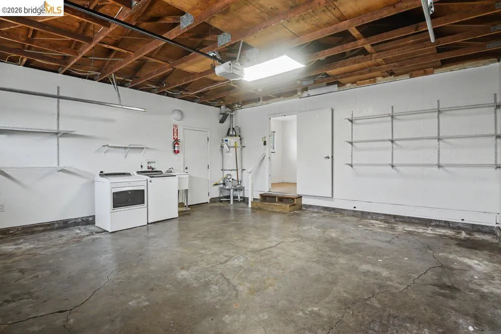 Exposed wood beam ceiling, concrete flooring, built-in shelving, utility sink, and a water heater