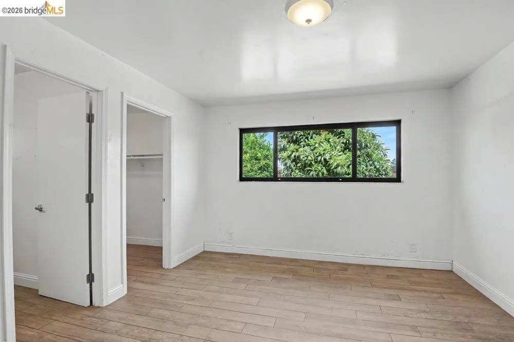 White walls with wood-finish flooring, a flush-mount ceiling light, and a window with black trim