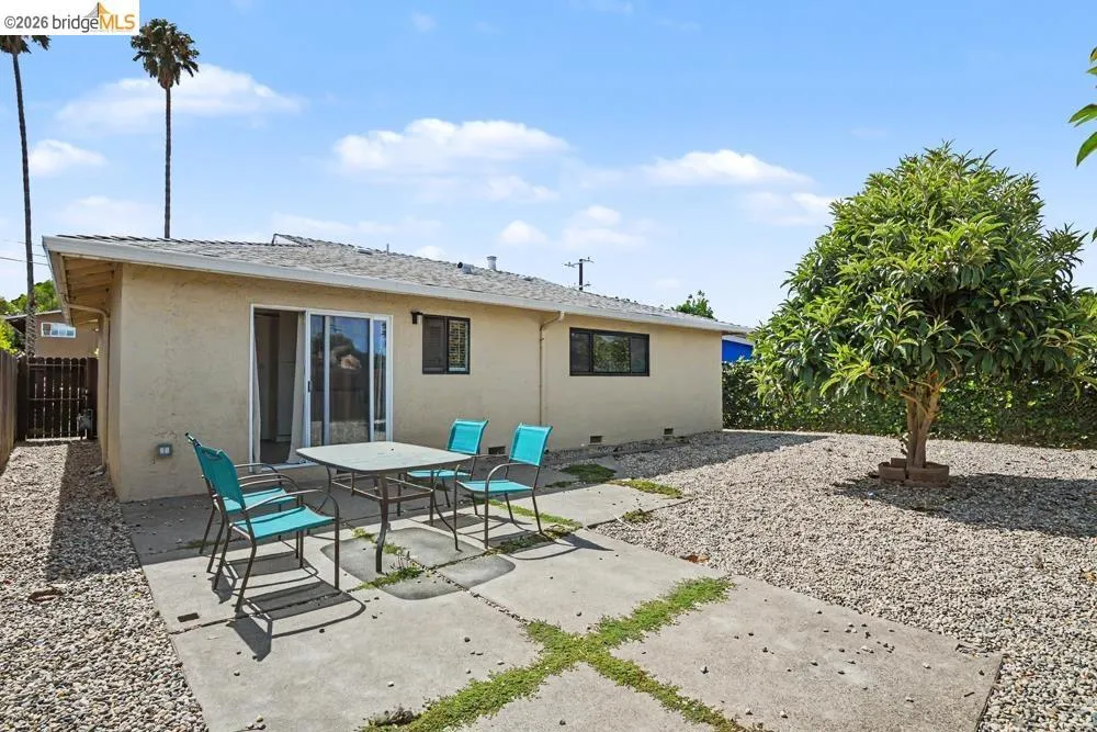 Expansive outdoor space featuring a concrete patio, gravel landscaping, mature trees, and a sliding glass door entry