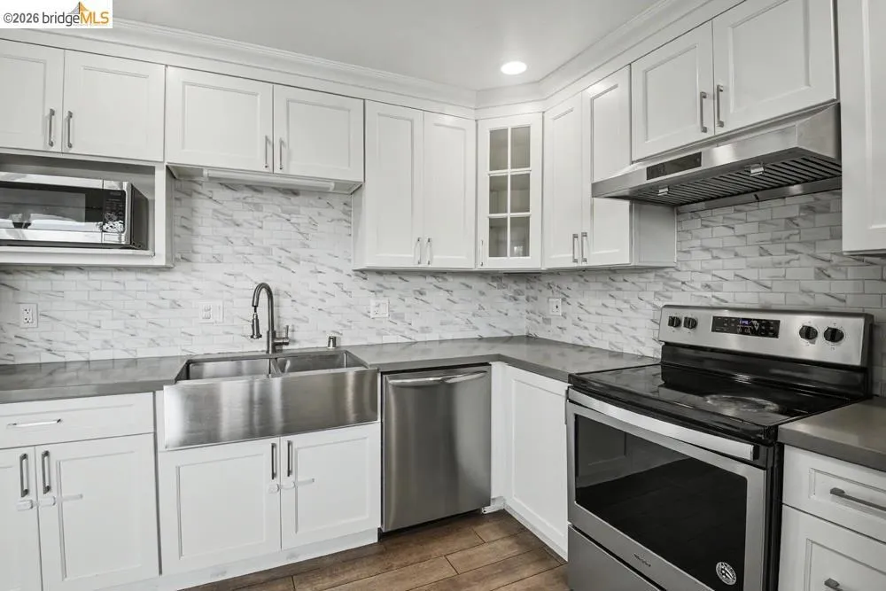 Kitchen featuring white shaker cabinetry, stainless steel appliances, a farmhouse-style sink, and a tiled backsplash