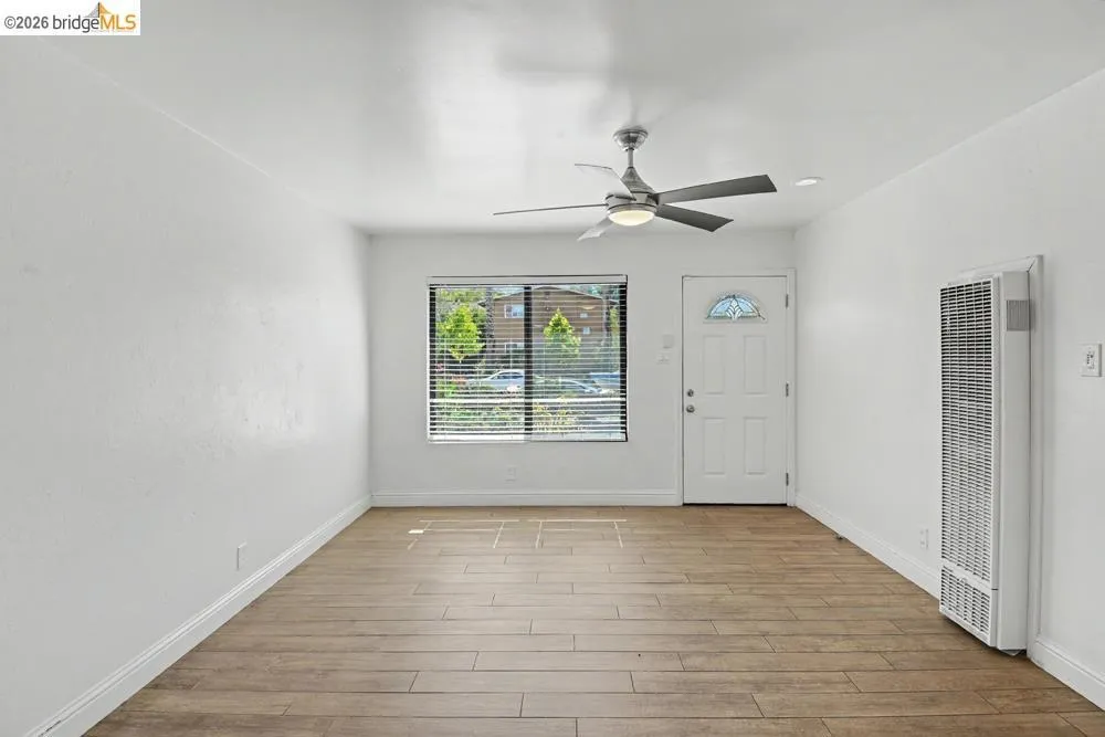 Wood-finish flooring, white walls, ceiling fan, and a front entry door with decorative glass