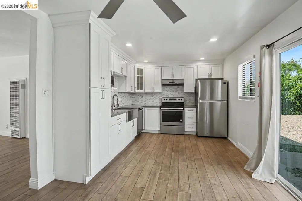 White shaker cabinetry with crown molding, stainless steel appliances, wood-finish flooring, recessed lighting, and a stainless steel farmhouse sink
