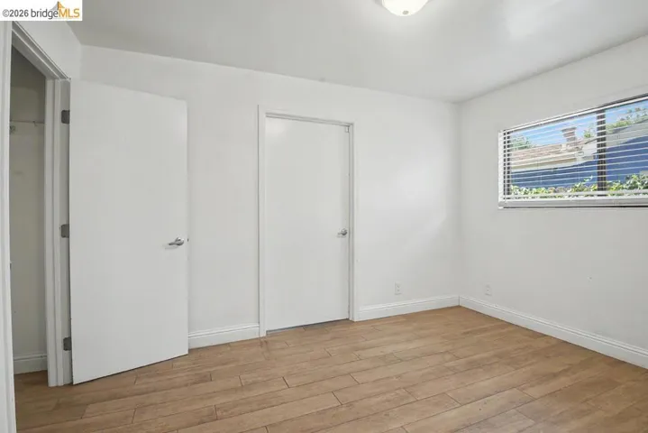 Wood-finish flooring, white walls, and a fixed window with horizontal blinds