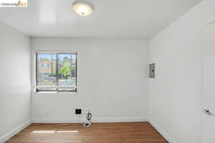 Wood-finish flooring with white baseboards, a window with blinds, and a flush-mount ceiling light