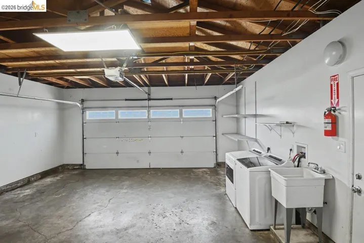 Exposed wood beam ceiling with recessed lighting, white garage door with upper-level windows, wall-mounted shelving, and utility sink