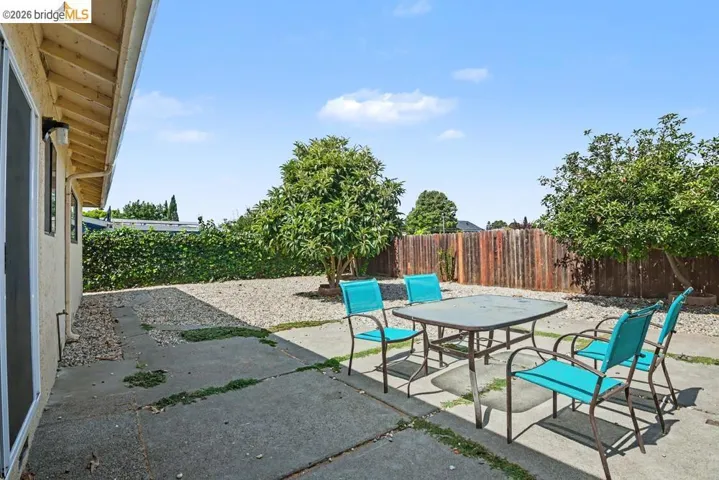 Concrete patio with gravel landscaping, surrounded by mature trees and a privacy fence