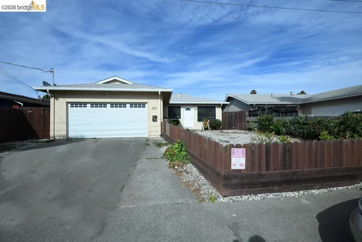 Single-story residence featuring light-colored siding, an attached garage with a white door, and a fenced front yard with plantings