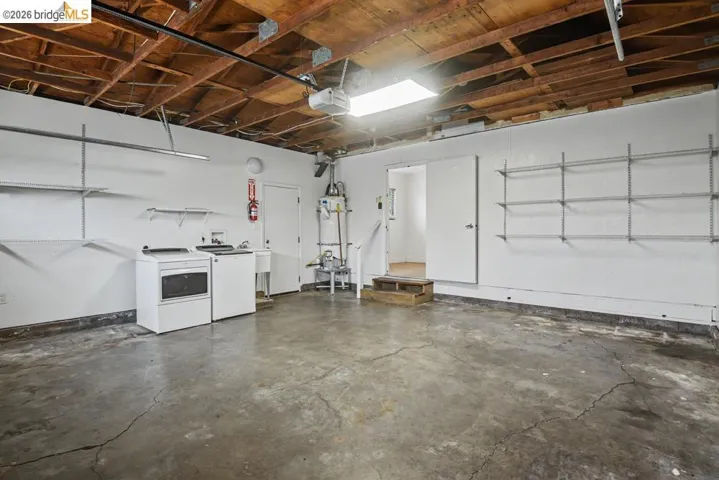 Exposed wood beam ceiling, concrete flooring, built-in shelving, utility sink, and a water heater