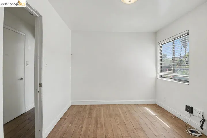 Wood-finish flooring, white walls, flush mount ceiling light, window with blinds, and white trim