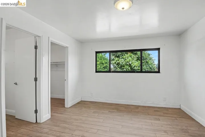 White walls with wood-finish flooring, a flush-mount ceiling light, and a window with black trim