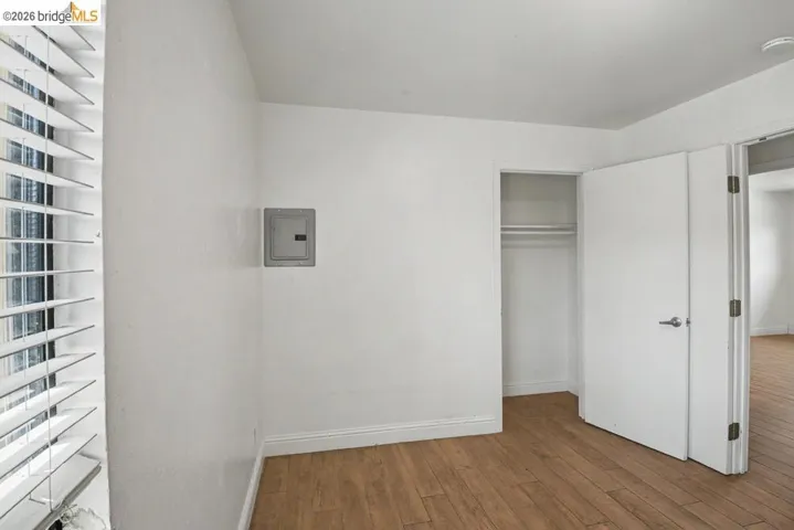 Wood-finish flooring, white horizontal blinds, and a built-in closet with a hanging rod