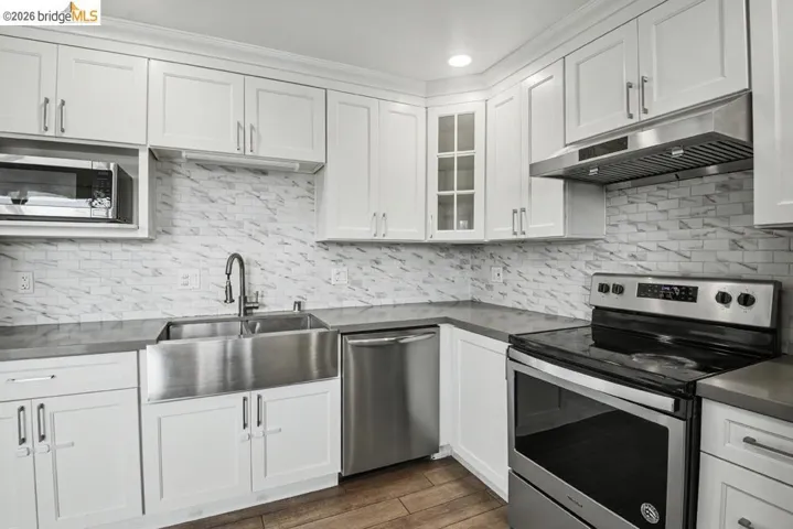 Kitchen featuring white shaker cabinetry, stainless steel appliances, a farmhouse-style sink, and a tiled backsplash