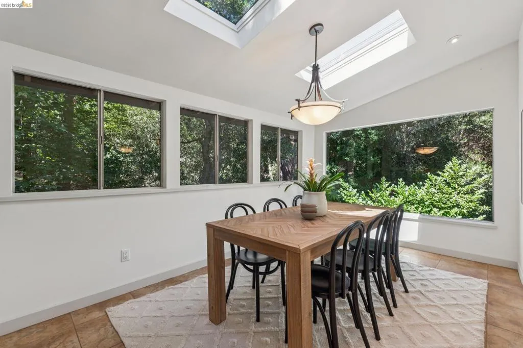 Vaulted ceilings with skylights, large picture window, multiple transom windows, suspended ceiling light fixture, and tile flooring