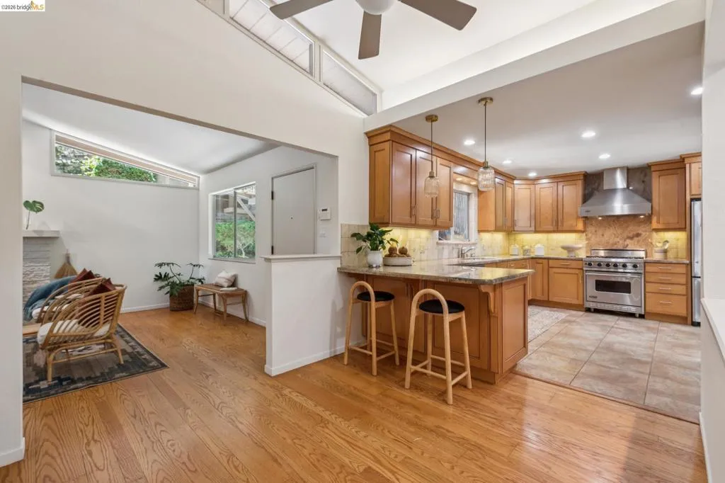 Hardwood flooring, wood cabinetry, stone countertops, stainless steel appliances, and a vaulted ceiling