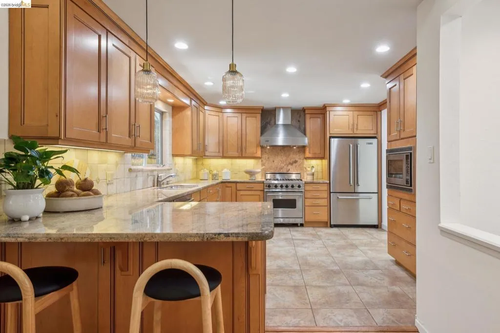 Warm wood cabinetry with recessed lighting, stainless steel appliances, granite countertops, and tile flooring