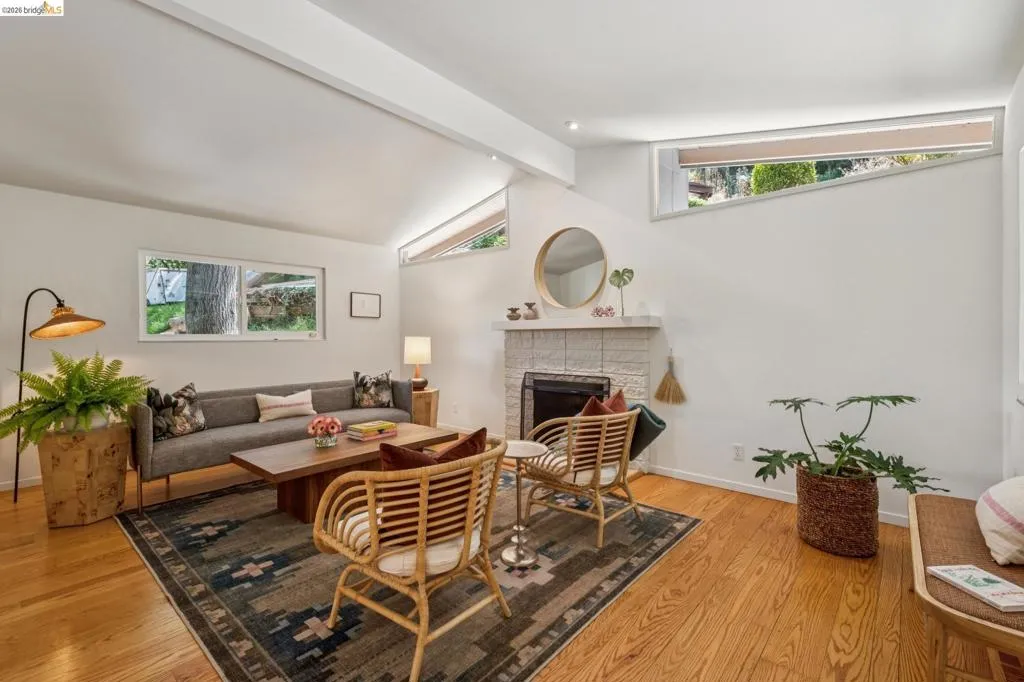 Vaulted ceiling, wood-finish flooring, white painted walls, fireplace with tile surround, and horizontal windows