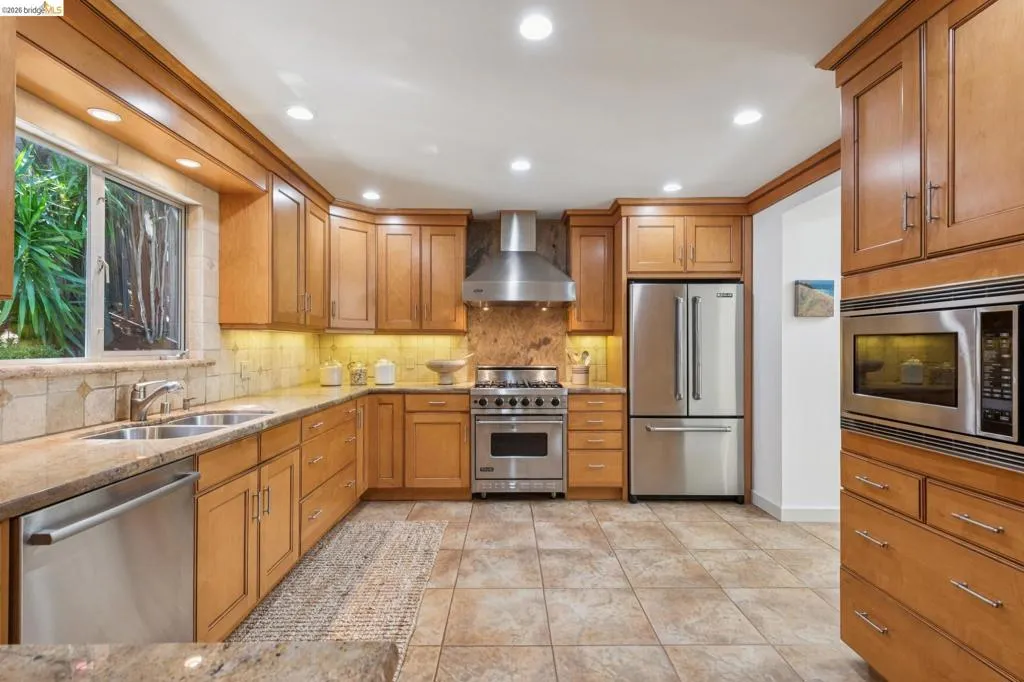Stainless steel appliances, recessed ceiling lighting, wood cabinetry, stone countertops, and tile flooring