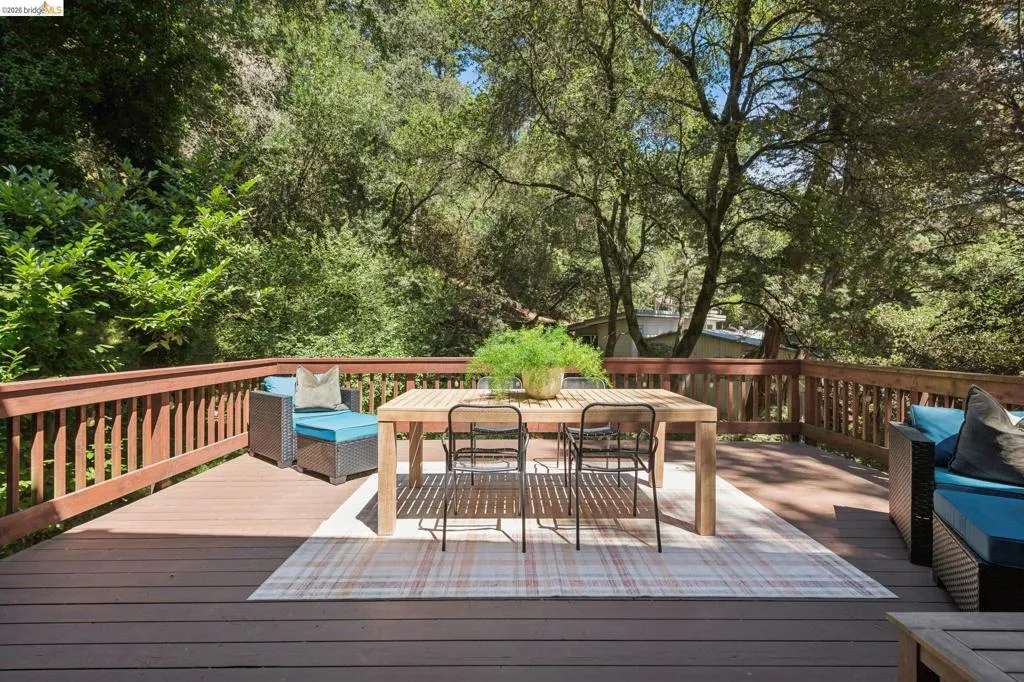 Expansive outdoor deck featuring composite decking, wood railing, and a mature treed backdrop