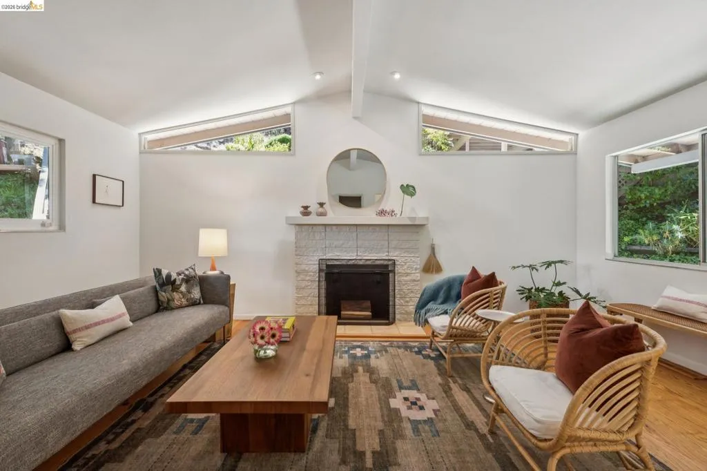Vaulted ceiling with exposed beam, stone-tiled fireplace with hearth, and multiple windows providing natural light