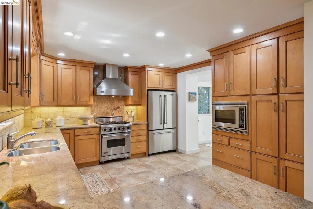 Wood-finish cabinetry with stainless steel appliances, recessed lighting, stone countertops, and tile flooring