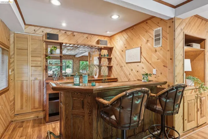 Built-in wood-paneled wet bar with integrated shelving, storage cabinetry, and wood-finish flooring