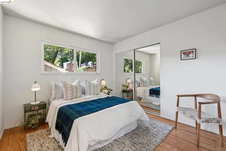 Wood-finish flooring, white walls, horizontal window, and mirrored closet doors
