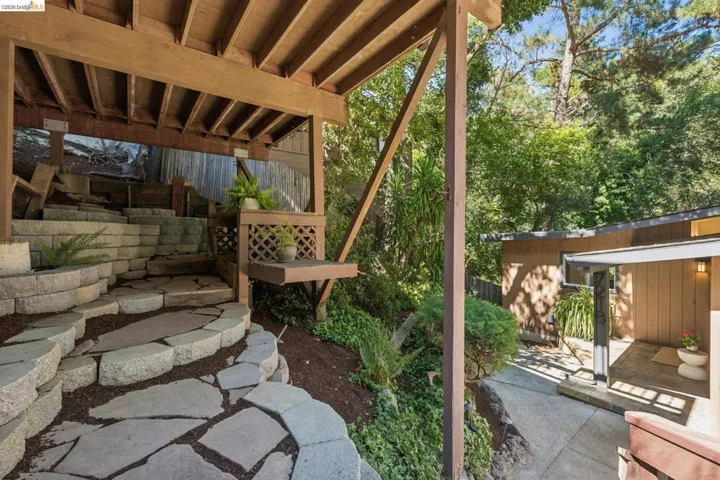 Layered stone retaining walls, flagstone steps, wood beam construction, latticework detailing, and a sloped, planted garden bed