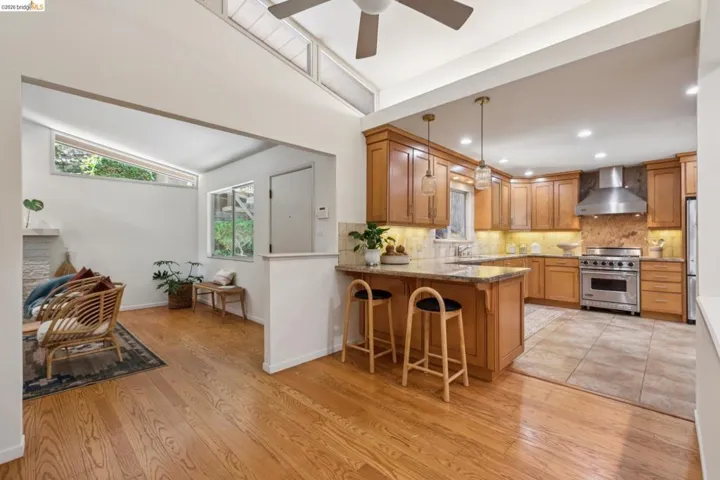 Hardwood flooring, wood cabinetry, stone countertops, stainless steel appliances, and a vaulted ceiling