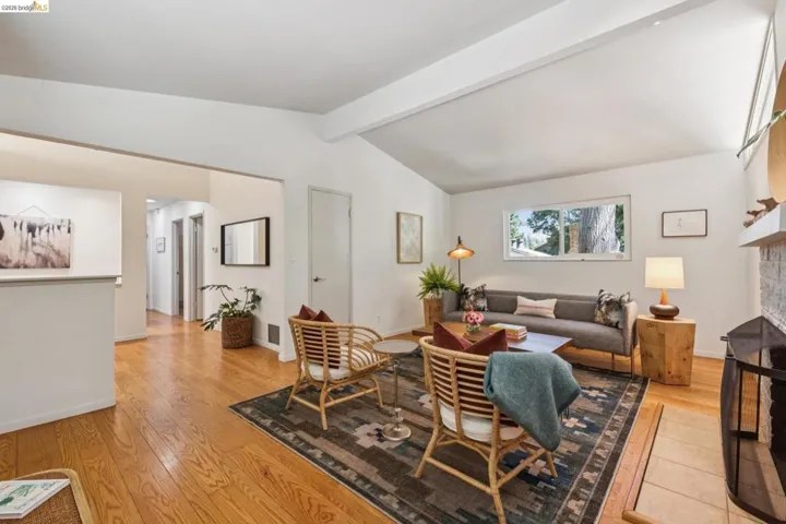 Vaulted ceiling with exposed beams, wood-finish flooring, white painted walls, and a fireplace with a hearth