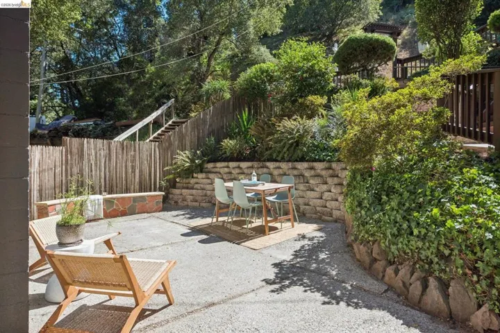 Expansive outdoor patio with concrete paving, wood fencing, and a terraced hillside garden