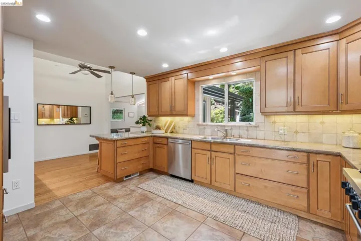 Recessed lighting illuminates wood cabinetry, stainless steel appliances, and a tiled backsplash