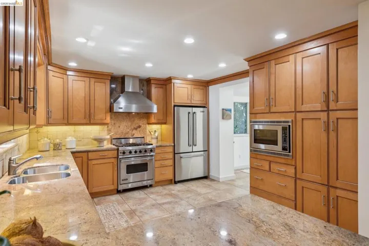 Wood-finish cabinetry with stainless steel appliances, recessed lighting, stone countertops, and tile flooring