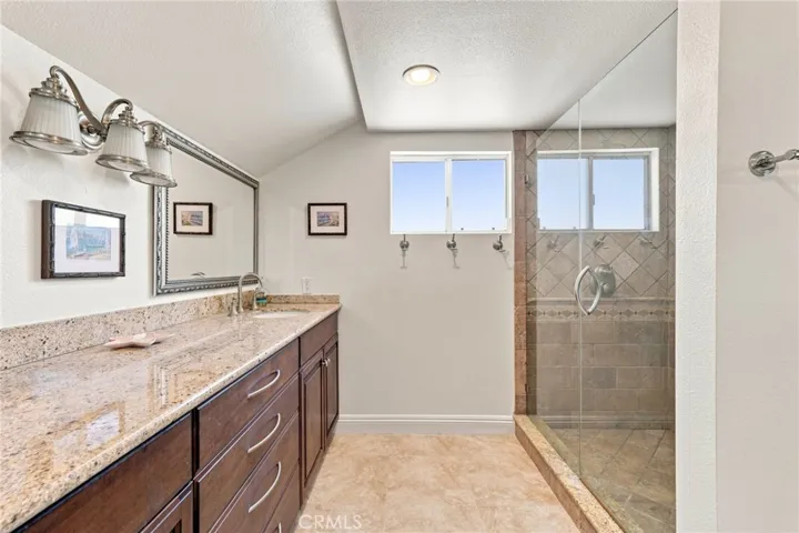 The upgraded primary bath features dual sinks, granite countertops, updated cabinetry, and a large custom finished walk-in shower with glass enclosure.
