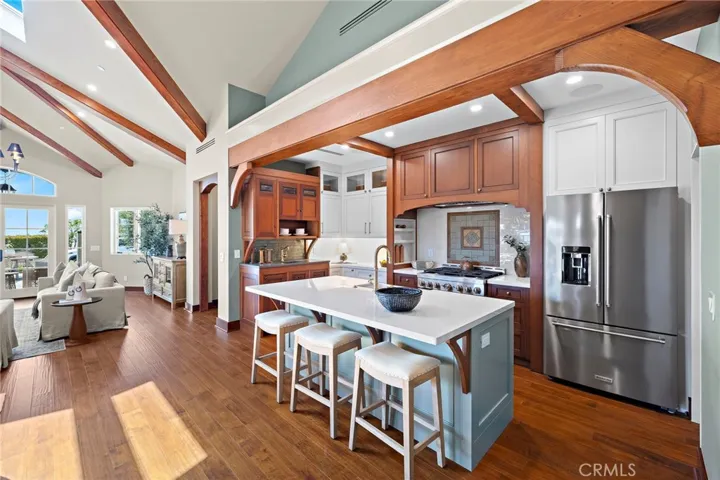 Custom kitchen features reclaimed Honduras mahogany cabinetry, quartz countertops, a farmhouse sink, high-end appliance package, and a handmade tile backsplash behind the range.