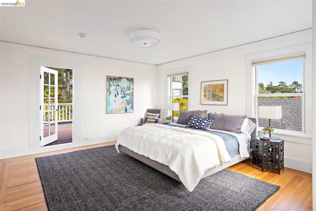 Light-filled room featuring wood-finish flooring, multiple windows, a ceiling-mounted light fixture, and double French doors opening to an exterior deck with white railings Light-filled room featuring wood-finish flooring, multiple windows, a ceiling-mounted light fixture, and double French doors opening to an exterior deck with white railings