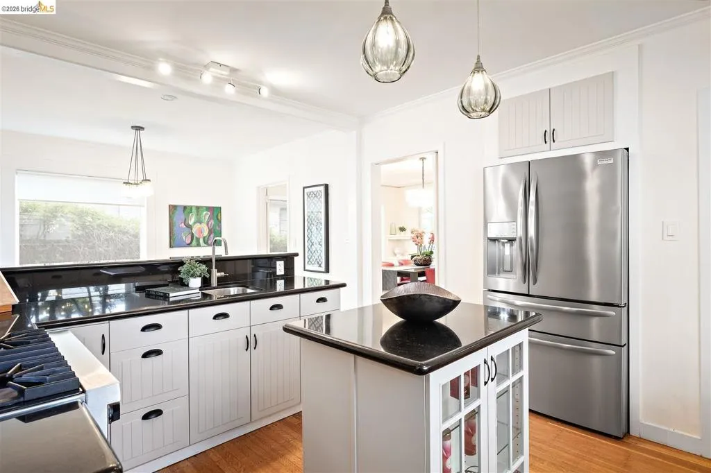 Kitchen featuring a stainless steel refrigerator, white cabinetry, a kitchen island with storage, pendant lighting, and dark countertops Kitchen featuring a stainless steel refrigerator, white cabinetry, a kitchen island with storage, pendant lighting, and dark countertops