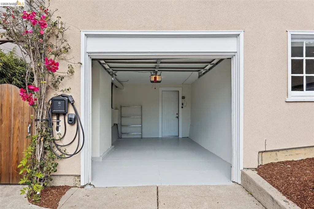 Attached garage featuring an electric vehicle charging station, painted concrete flooring, and an interior access door Attached garage featuring an electric vehicle charging station, painted concrete flooring, and an interior access door
