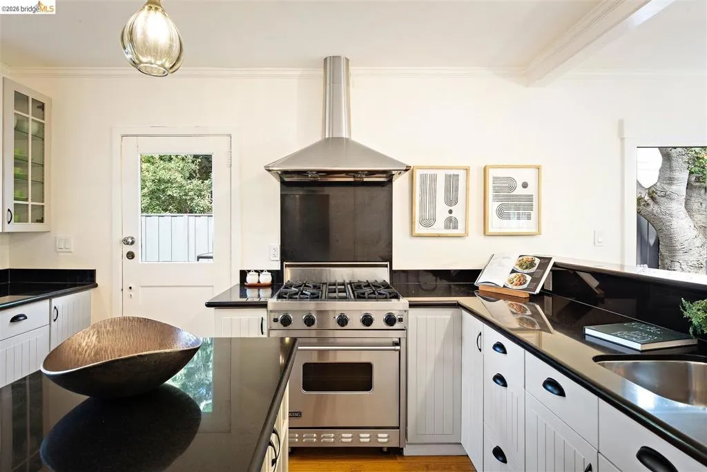 Stainless steel range with a professional-grade hood, black countertops, white shaker-style cabinetry, and a glass-paneled back door Stainless steel range with a professional-grade hood, black countertops, white shaker-style cabinetry, and a glass-paneled back door