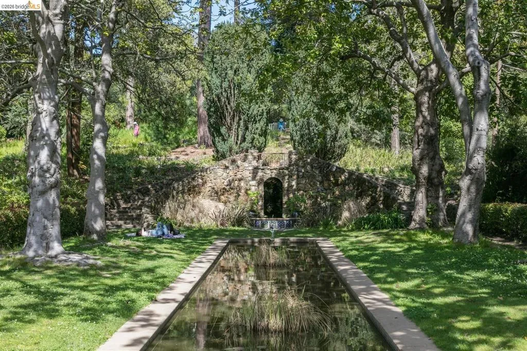 Manicured lawn with a rectangular reflecting pool, mature trees, and a stone-built retaining wall with a water feature Manicured lawn with a rectangular reflecting pool, mature trees, and a stone-built retaining wall with a water feature