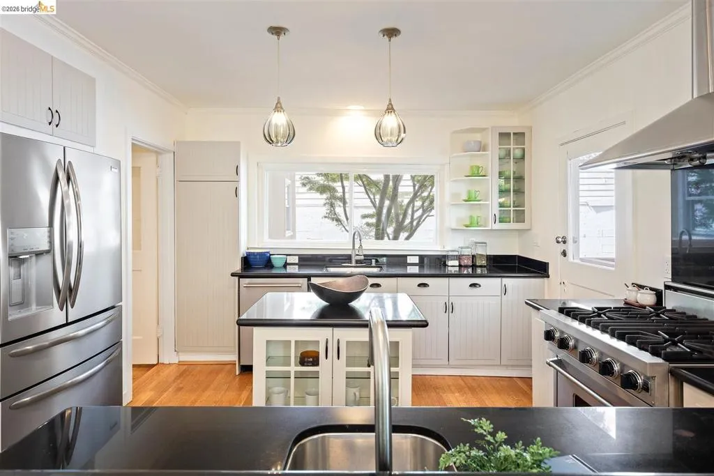 Kitchen featuring wood-finish flooring, white cabinetry, black countertops, and stainless steel appliances Kitchen featuring wood-finish flooring, white cabinetry, black countertops, and stainless steel appliances