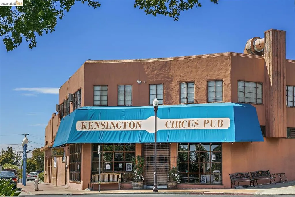 Two-story commercial building featuring stucco exterior, prominent blue awning, multiple large windows, and street-level access Two-story commercial building featuring stucco exterior, prominent blue awning, multiple large windows, and street-level access