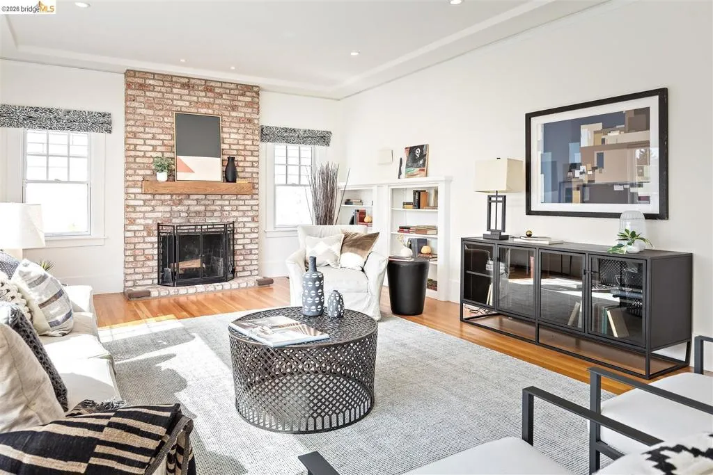 Bright living room anchored by a brick fireplace with dark surround and hearth, hardwood flooring throughout, recessed ceiling lighting, and built-in media console with shelving Bright living room anchored by a brick fireplace with dark surround and hearth, hardwood flooring throughout, recessed ceiling lighting, and built-in media console with shelving