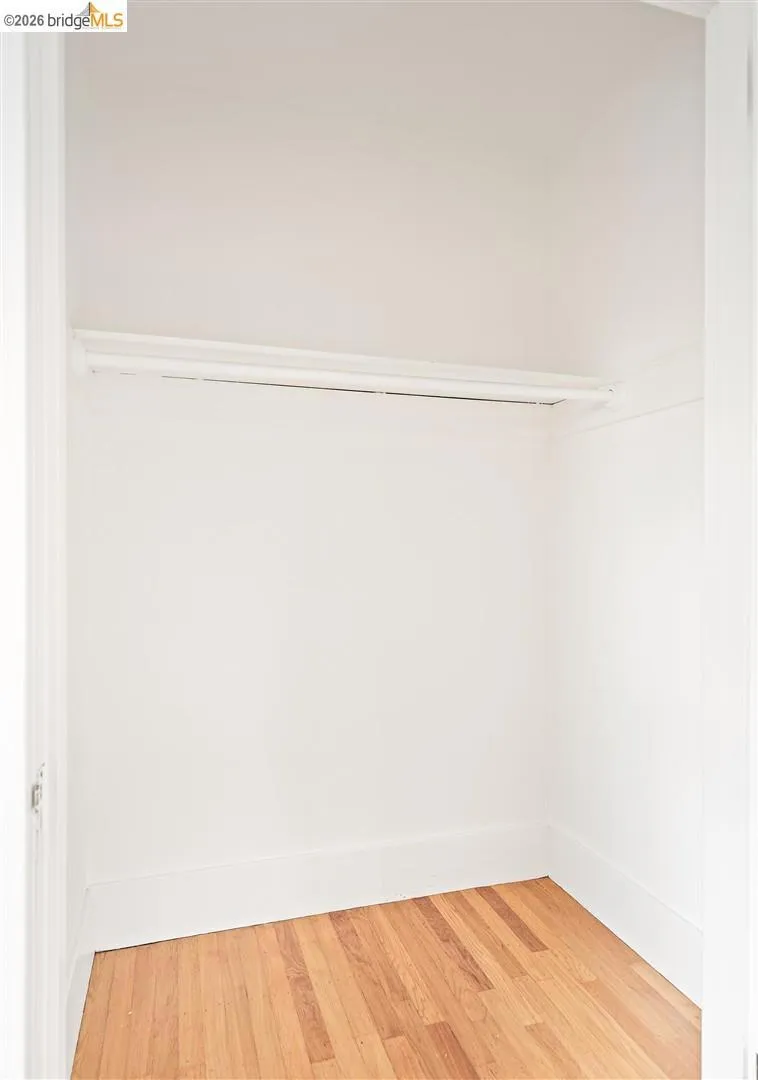 Closet space featuring wood-finish flooring and a built-in hanging rod Closet space featuring wood-finish flooring and a built-in hanging rod