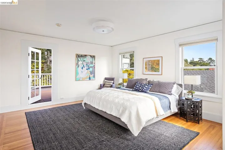 Light-filled room featuring wood-finish flooring, multiple windows, a ceiling-mounted light fixture, and double French doors opening to an exterior deck with white railings