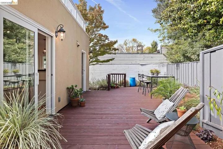 Expansive outdoor deck with rich wood-finish flooring, featuring a stucco exterior with an outdoor wall sconce