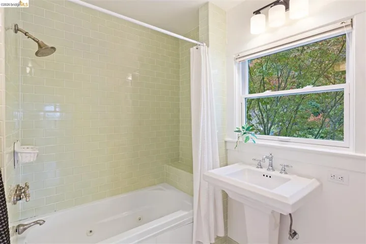 Pedestal sink with chrome fixtures, tiled bathtub surround, and a double-hung window