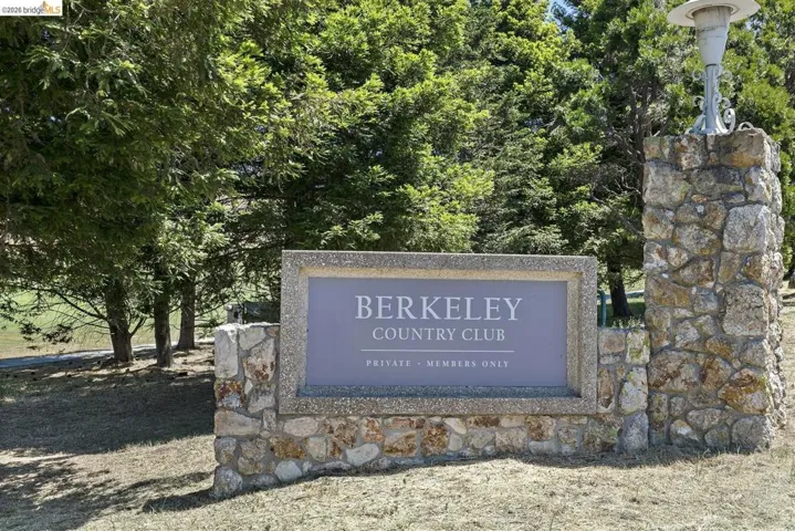 Stone-clad entrance sign with a decorative light fixture, surrounded by mature trees and natural landscaping