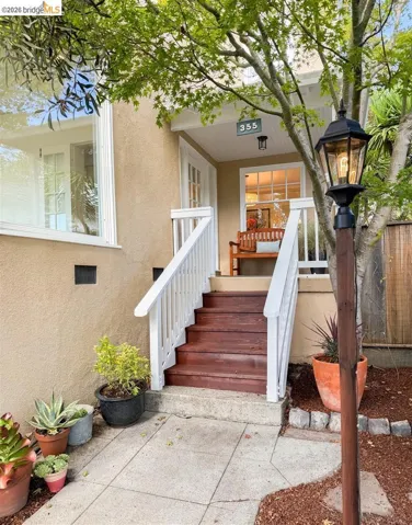 Covered front porch with white railings, wood-finish steps, and an exterior sconce